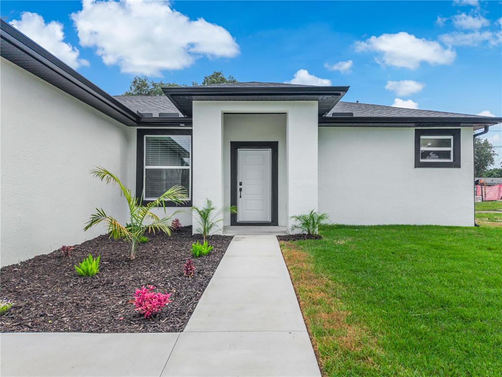 A white house with black trim features a garage, front entrance, and landscaped garden bed — 222 FLORIDA AVENUE, DUNDEE, FL
