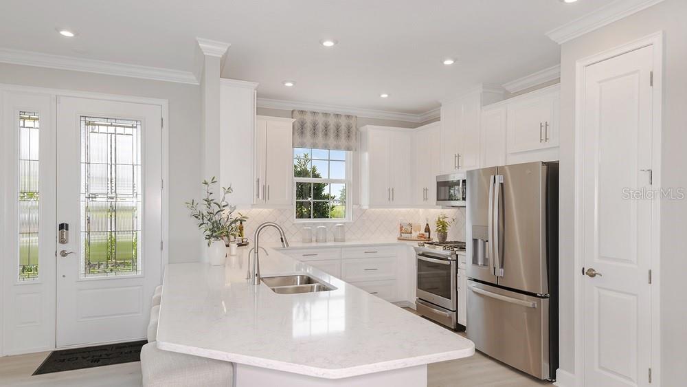 A modern kitchen features white cabinetry, quartz countertops, stainless steel appliances, and a large island — 7452 MOONBEAM AVENUE, SARASOTA, FL