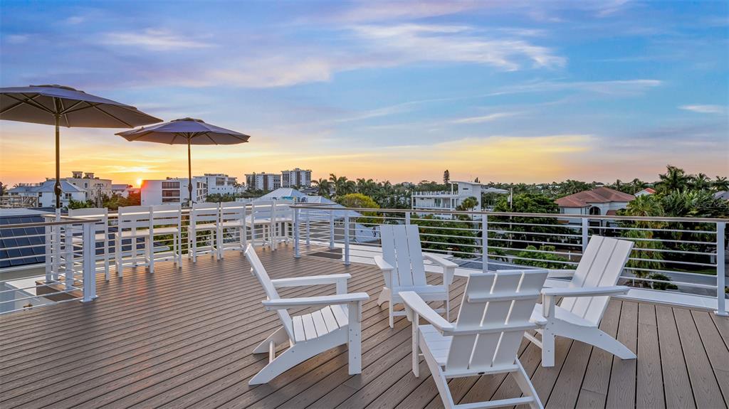 A rooftop deck features white Adirondack chairs, high-top seating, and umbrellas at sunset — 161 TYLER DRIVE, SARASOTA, FL