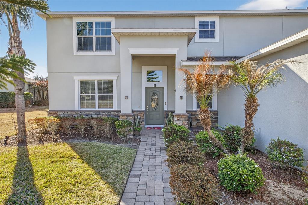 A two-story house exterior features a stone-accented facade, a paved walkway, and palm trees — 1336 LATTIMORE DRIVE, CLERMONT, FL