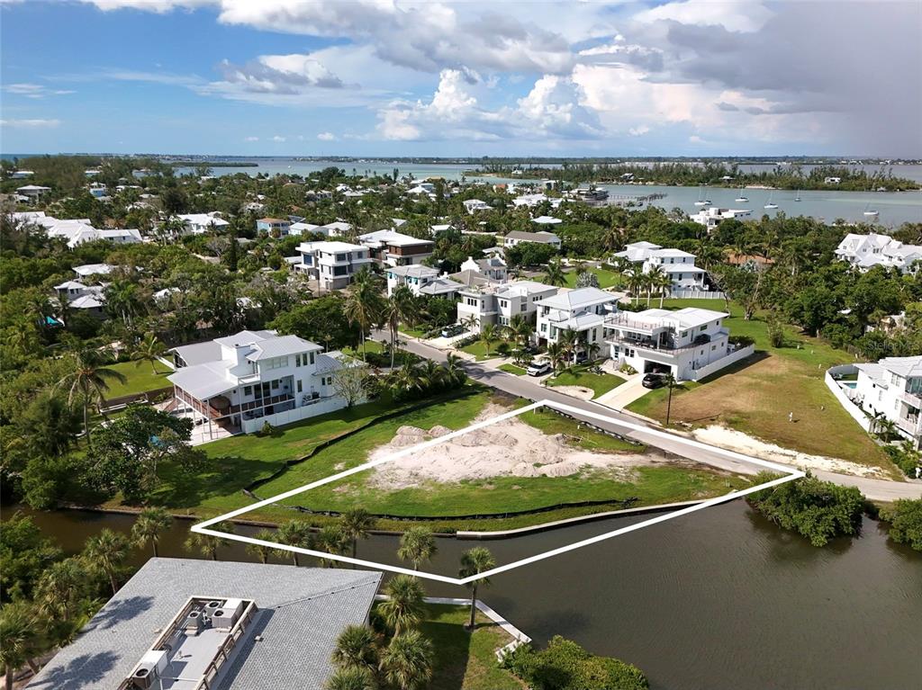 An aerial view shows a vacant waterfront lot outlined in white near a residential neighborhood — 6801 LONGBOAT DRIVE S, LONGBOAT KEY, FL