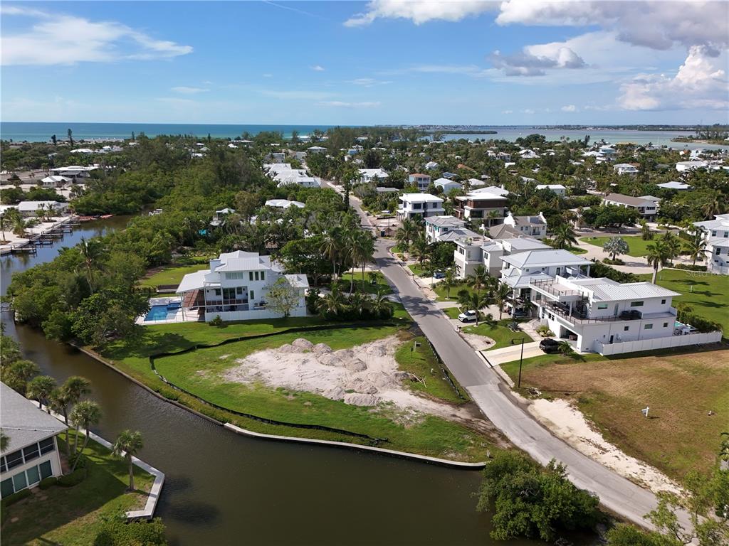 An aerial view shows a coastal neighborhood with houses, a canal, and a vacant lot — 6801 LONGBOAT DRIVE S, LONGBOAT KEY, FL