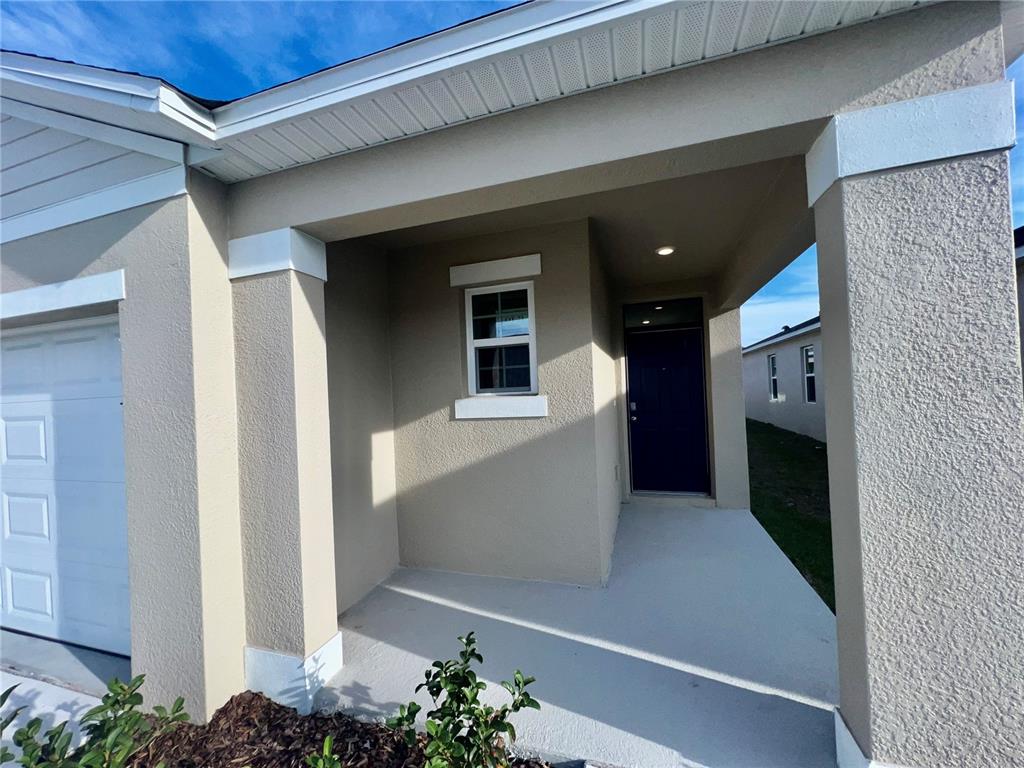 The exterior view shows a covered front porch with a dark blue door and window — 7086 CATTLE EGRET DRIVE, HARMONY, FL