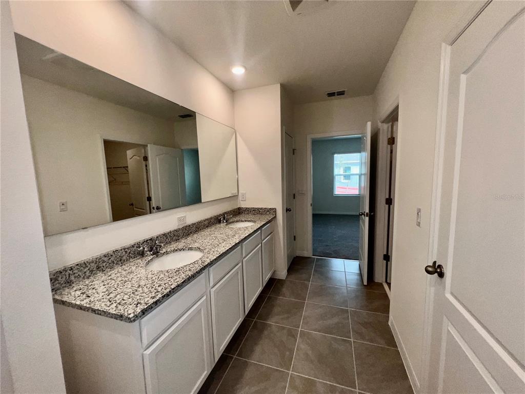 A bathroom features a double-sink granite vanity with white cabinets and a large wall mirror — 7086 CATTLE EGRET DRIVE, HARMONY, FL