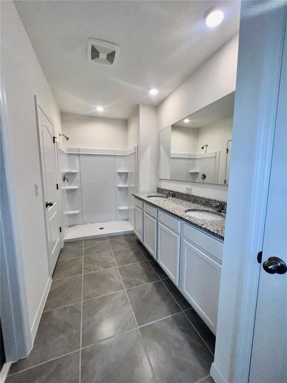 A bathroom with a walk-in shower, double vanity, granite countertops, and gray tile flooring — 7086 CATTLE EGRET DRIVE, HARMONY, FL