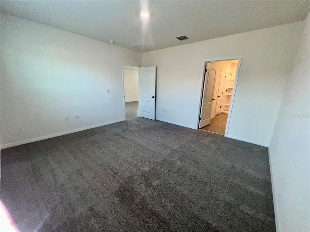 A carpeted bedroom features two white doors leading to an adjacent room and a bathroom — 7086 CATTLE EGRET DRIVE, HARMONY, FL