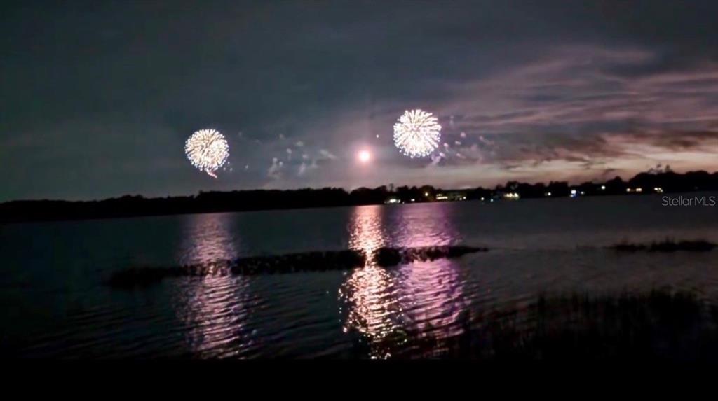 Fireworks explode over a dark lake at night with reflections visible on the water — 8822 WINTER GARDEN VINELAND ROAD, ORLANDO, FL