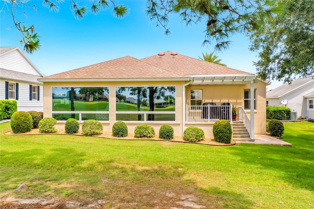 The rear exterior of a single-story house features large windows, a small patio, and landscaping — 268 LAWTHORN STREET, THE VILLAGES, FL