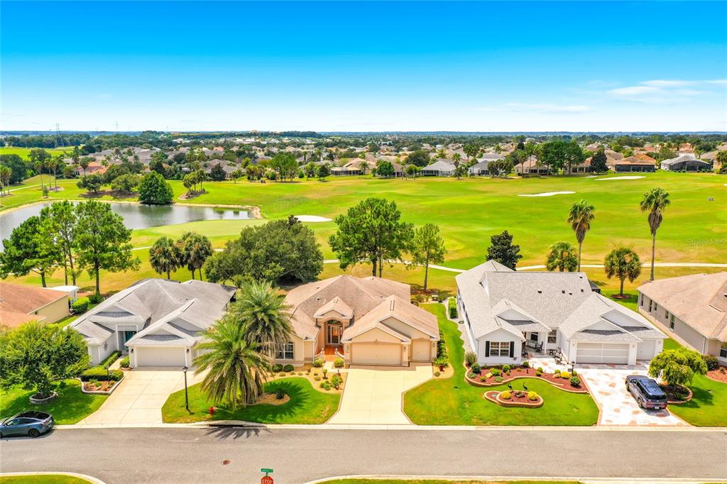 An aerial view shows three suburban houses situated along a golf course and pond — 268 LAWTHORN STREET, THE VILLAGES, FL