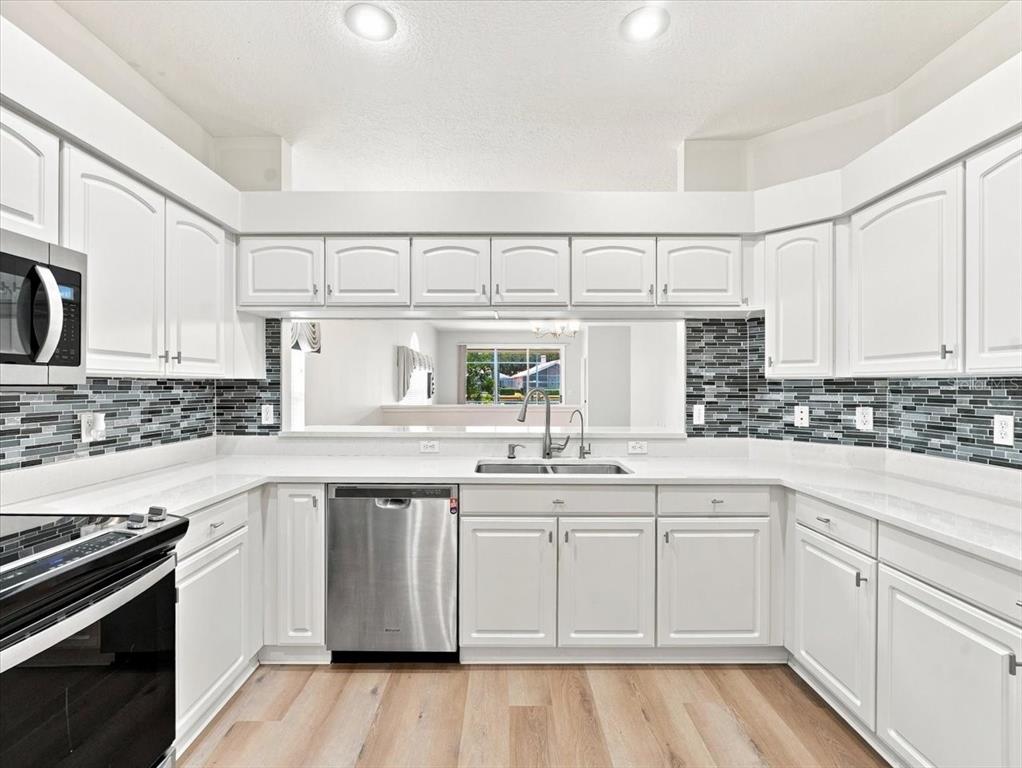 A kitchen with white cabinets, stainless steel appliances, and a gray and black tile backsplash — 1333 LINDENWOOD DRIVE, TARPON SPRINGS, FL