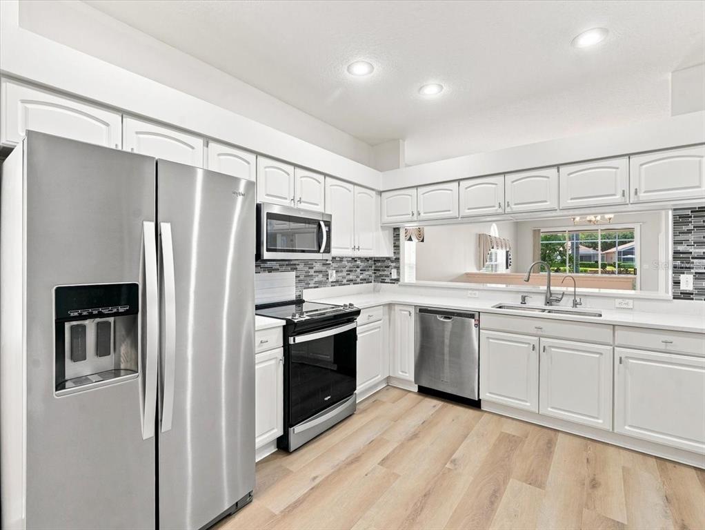A kitchen with white cabinets, stainless steel appliances, a tiled backsplash, and light floor tiles — 1333 LINDENWOOD DRIVE, TARPON SPRINGS, FL