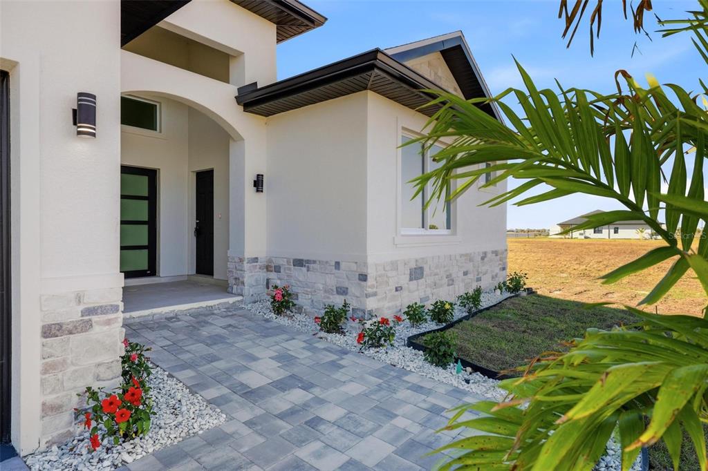A paved walkway leads to the covered entrance of a modern home with stone accents — 23 WREN DRIVE, PLACIDA, FL