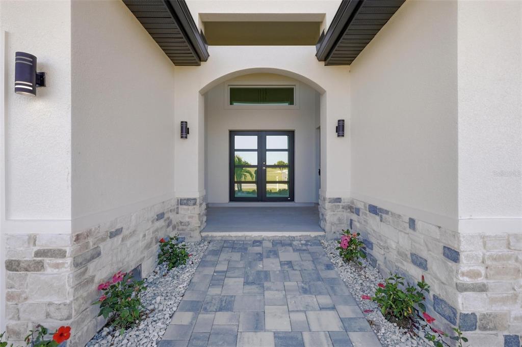 A paved walkway leads to the arched entryway of a home with double glass doors — 23 WREN DRIVE, PLACIDA, FL