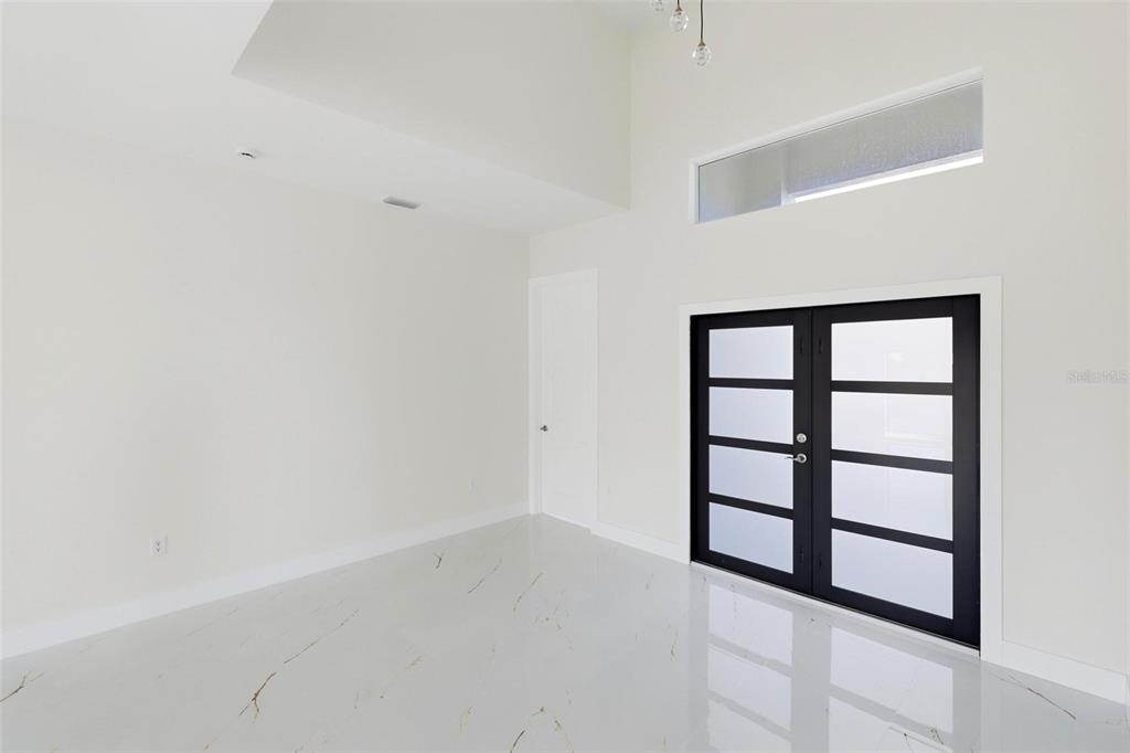 A bright room with white marble-look tile flooring, high ceilings, and black-framed double glass doors — 23 WREN DRIVE, PLACIDA, FL