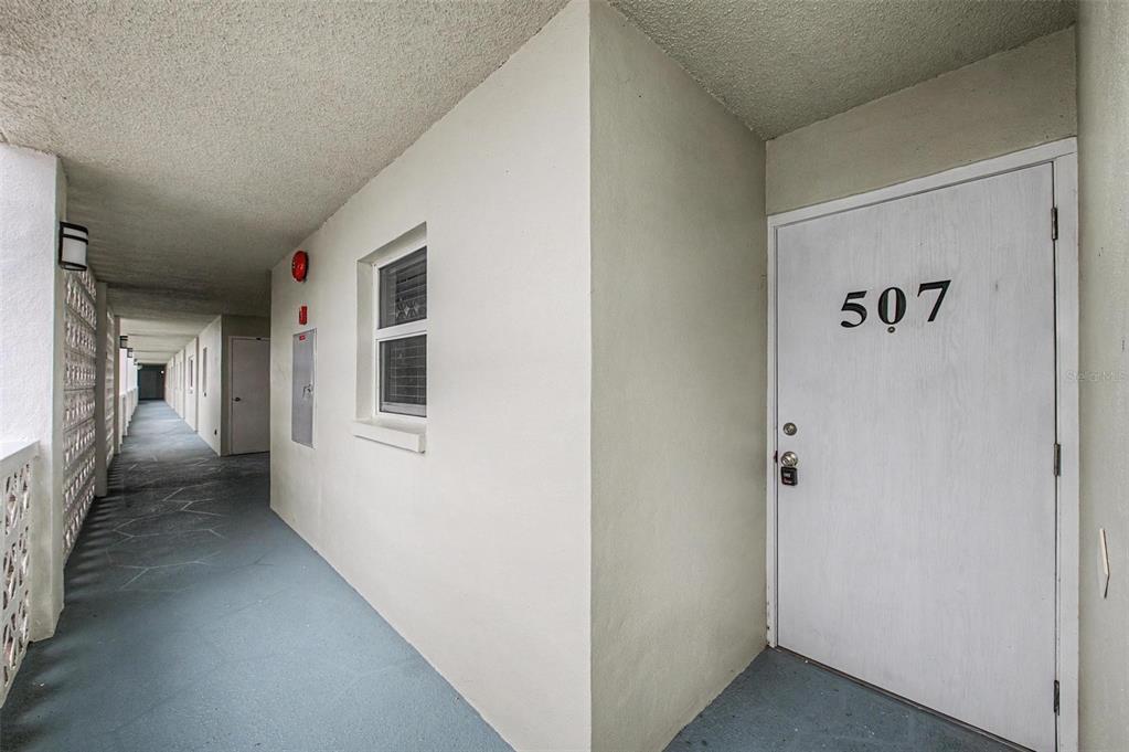 An exterior apartment hallway features a white door labeled 507 and a single window — 9 FORBES PLACE UNIT 507, DUNEDIN, FL