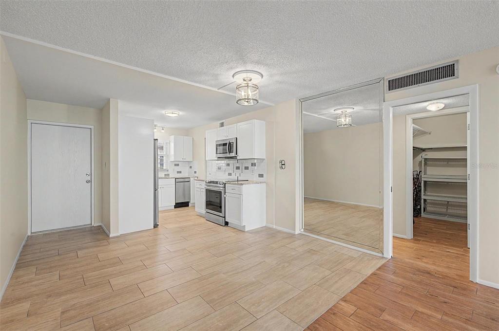 A kitchen with white cabinets and stainless steel appliances opens to a room with mirrors — 9 FORBES PLACE UNIT 507, DUNEDIN, FL