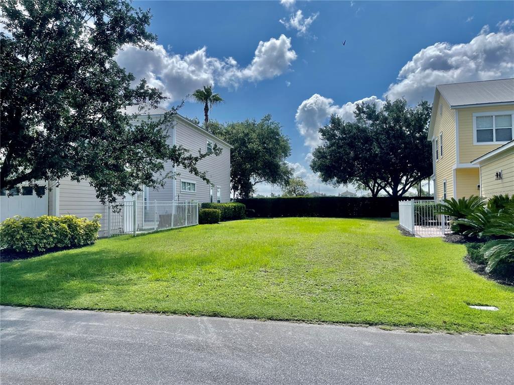 A grassy vacant lot sits between two suburban houses under a blue sky with clouds — 1436 REUNION BOULEVARD, REUNION, FL