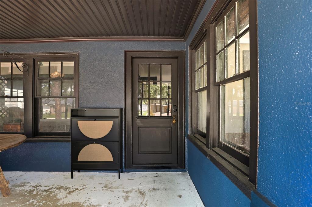 A covered porch features blue stucco walls, dark-trimmed windows, a glass-paneled door, and concrete flooring — 1510 WASHINGTON AVENUE, EUSTIS, FL