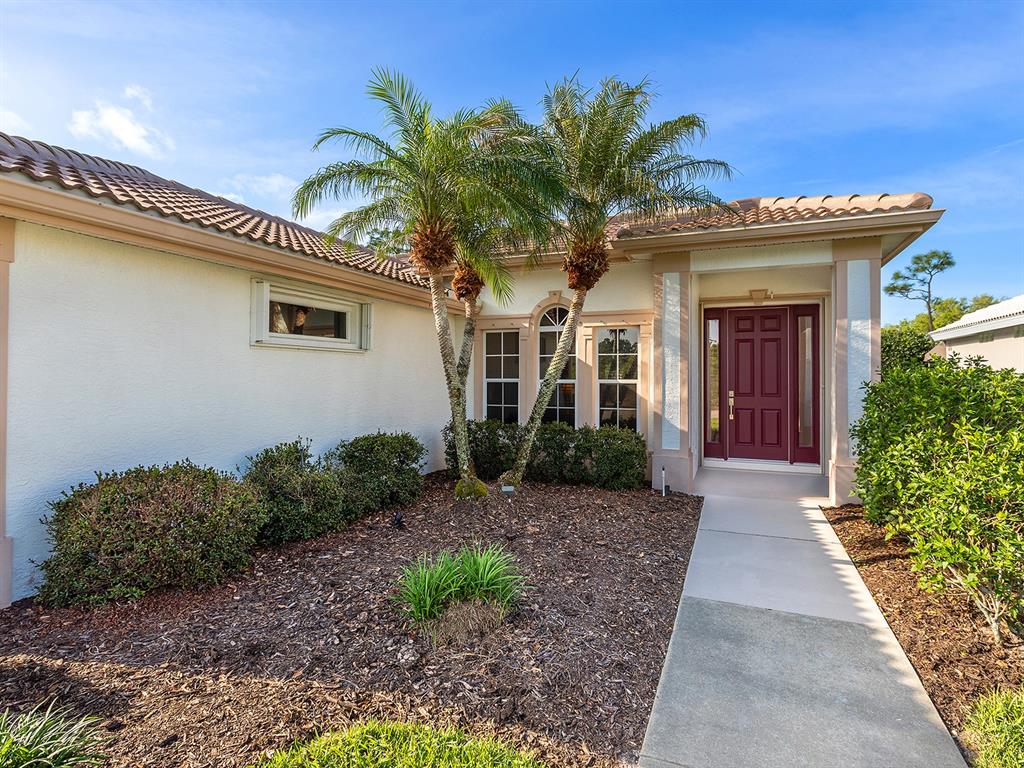 A single-story house exterior features a red front door, palm trees, and a concrete walkway — 10106 GLENMORE AVENUE, BRADENTON, FL