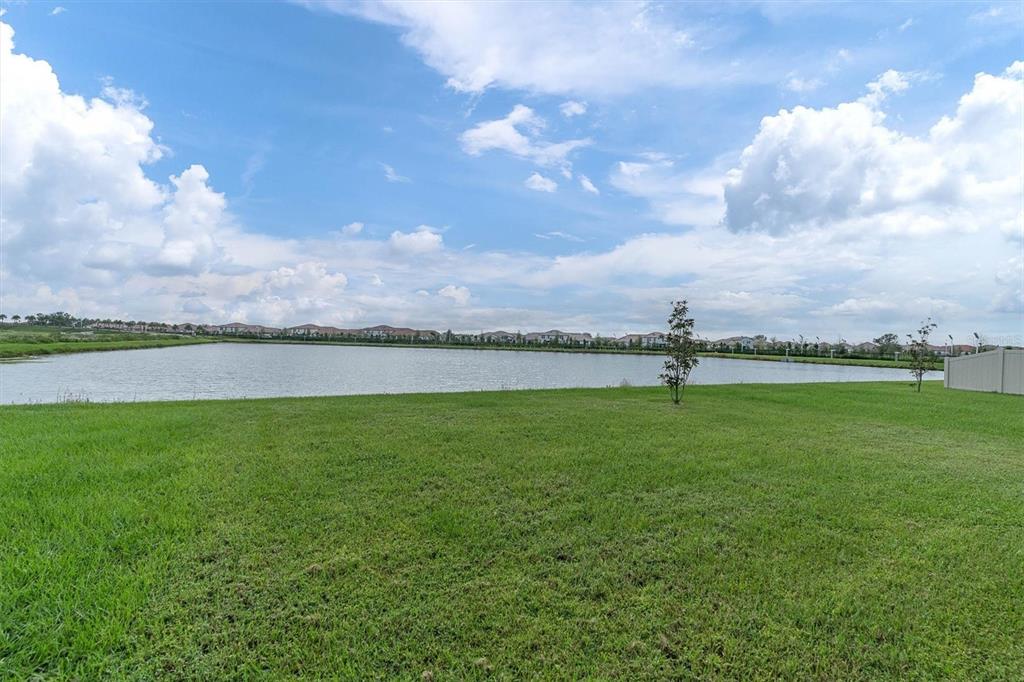 A grassy backyard overlooks a large pond with a residential neighborhood in the distance — 17070 OVAL RUM DRIVE, WIMAUMA, FL