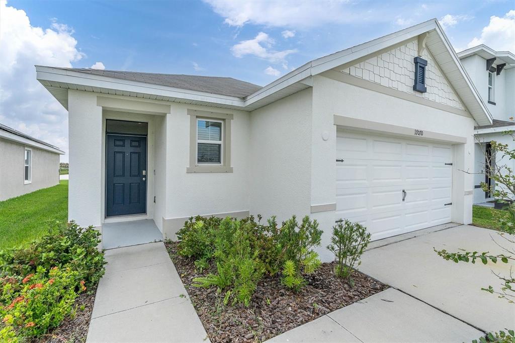 A single-story house with a white stucco exterior, blue front door, and a two-car garage — 17070 OVAL RUM DRIVE, WIMAUMA, FL