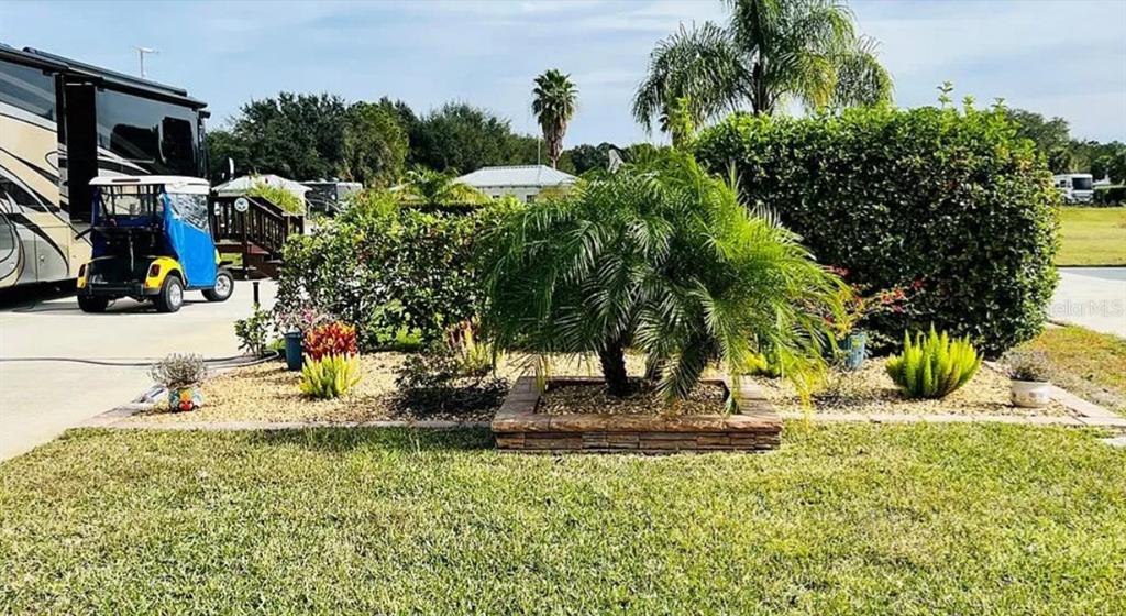 A golf cart is parked next to a motorhome near a landscaped garden with palm trees — 9531 SE 47TH WAY UNIT 280, WEBSTER, FL