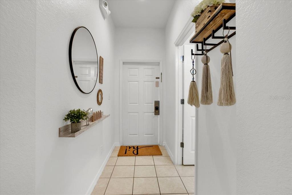 A bright entryway features a white door, tiled floor, wall-mounted shelf, and decorative wall hangings — 2783 CORVETTE LANE, KISSIMMEE, FL