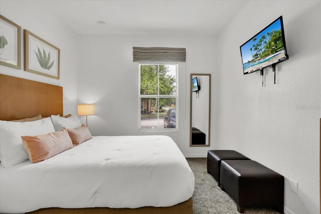 A bedroom features a bed, a window, a wall-mounted television, and two dark ottomans — 2783 CORVETTE LANE, KISSIMMEE, FL