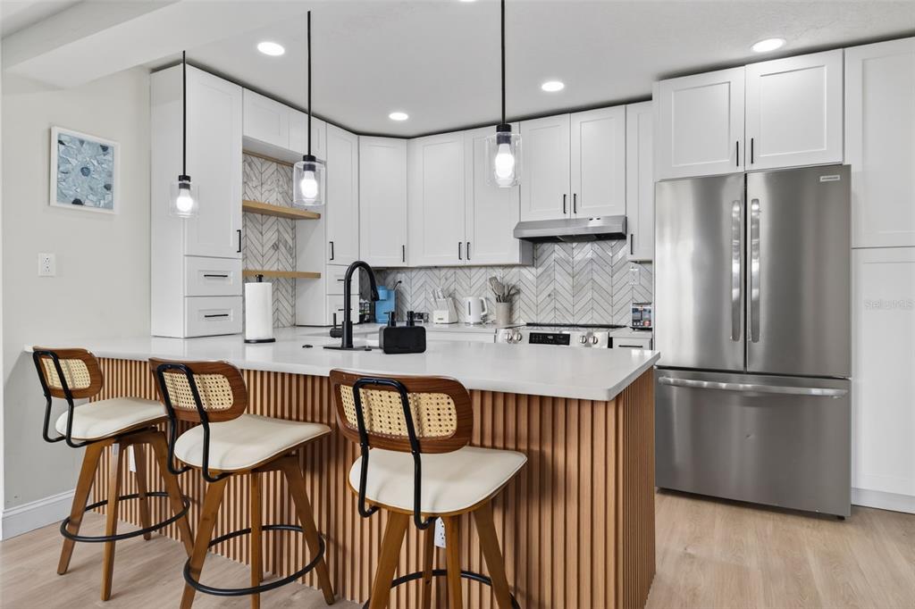 A modern kitchen features white cabinets, a wood-slatted island, and a herringbone tile backsplash — 510 79TH AVENUE, ST PETE BEACH, FL