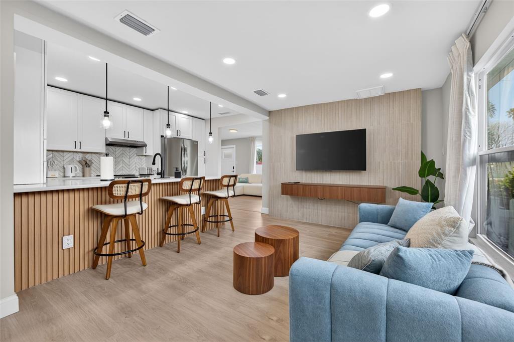 An open-concept living room and kitchen featuring a blue sofa, wood-slat island, and wall-mounted television — 510 79TH AVENUE, ST PETE BEACH, FL