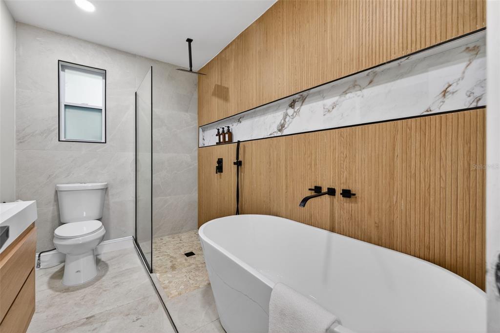 A modern bathroom features a freestanding tub, a glass-enclosed shower, and wood-slat wall paneling — 510 79TH AVENUE, ST PETE BEACH, FL