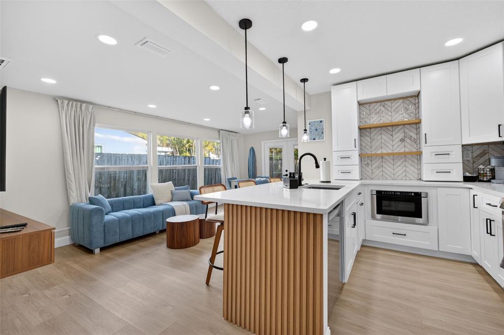 A kitchen with white cabinets and a wood-slatted island overlooks a living area with a sofa — 510 79TH AVENUE, ST PETE BEACH, FL