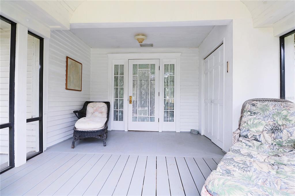 A covered porch features white siding, a glass-paneled front door, and two wicker chairs — 1109 CODY VILLA LOOP ROAD, BABSON PARK, FL