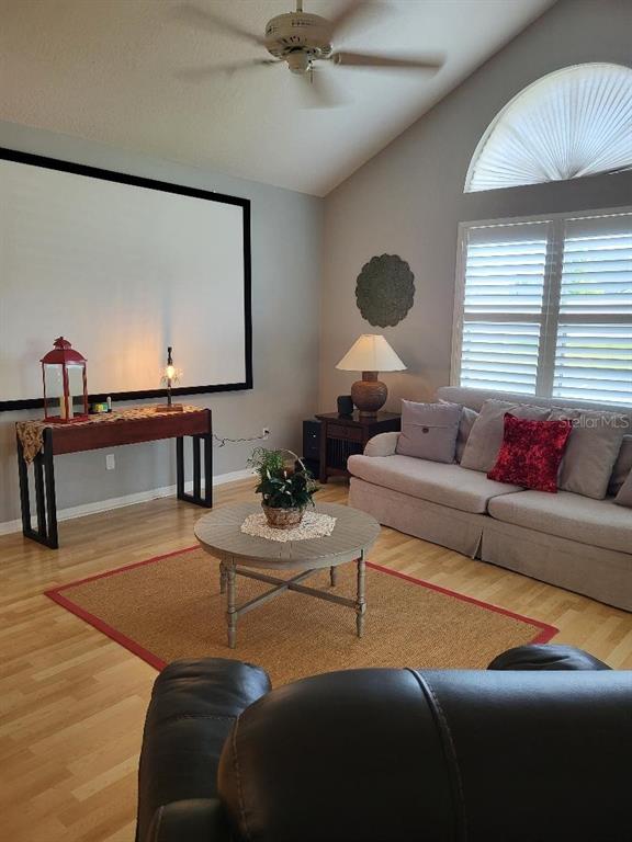 A living room features a large projector screen, light wood flooring, and a beige sofa — 3709 MOLLIE LANE, SUN CITY CENTER, FL