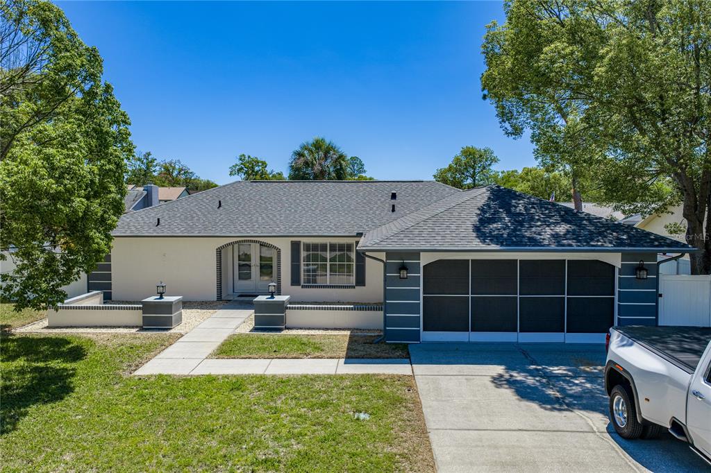A single-story house with a white stucco exterior, dark roof, and a screened-in garage door — 7435 KILBRIDE COURT, WEEKI WACHEE, FL
