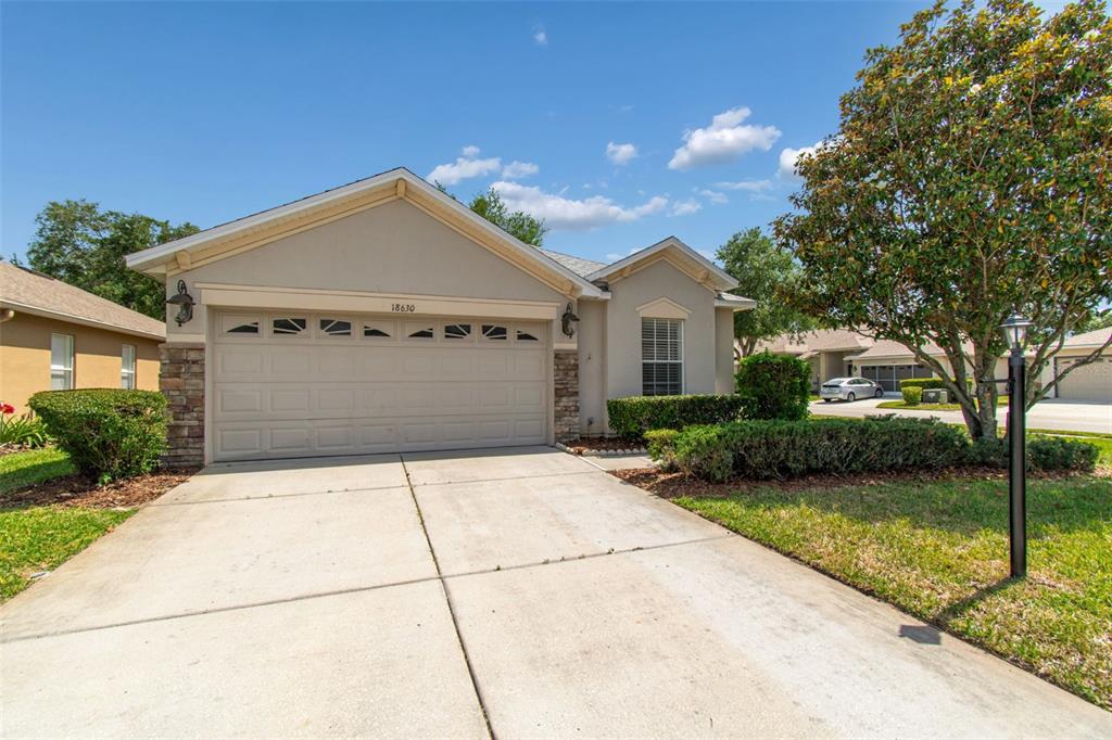 A single-story house with a beige stucco exterior, stone accents, and a two-car garage — 18630 ROLLING HILLS LOOP, HUDSON, FL