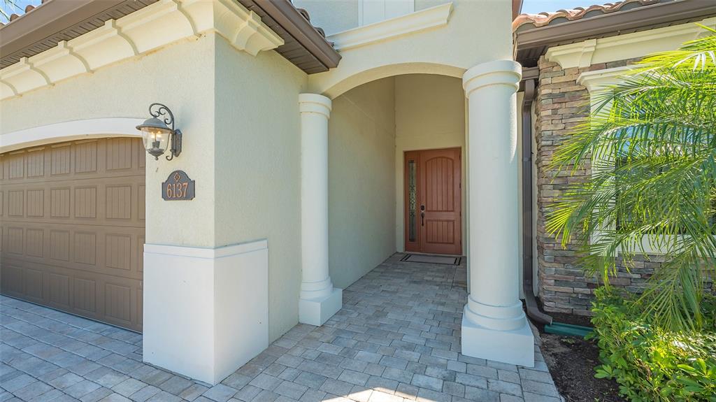 A house exterior features a paved walkway, two white columns, and a brown front door — 6137 CESSNA RUN, BRADENTON, FL