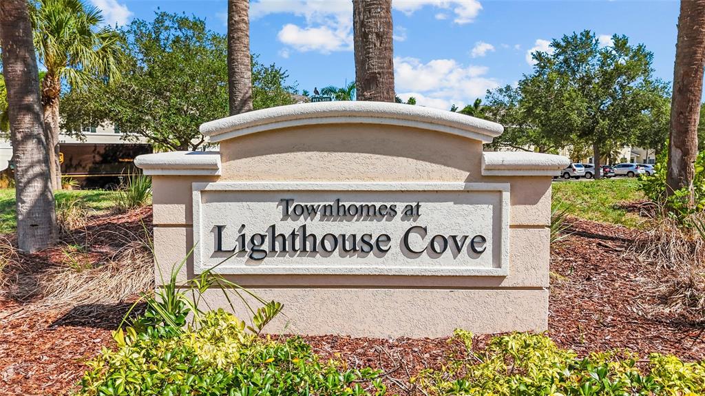 A beige monument sign for Townhomes at Lighthouse Cove stands outdoors surrounded by palm trees — 220 CAPE HARBOUR LOOP Unit 101, BRADENTON, FL