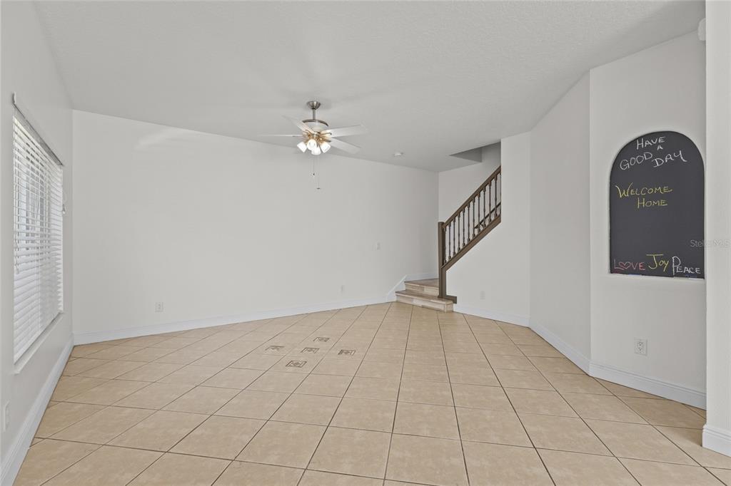An empty room features beige tile flooring, white walls, a ceiling fan, and a staircase — 220 CAPE HARBOUR LOOP Unit 101, BRADENTON, FL