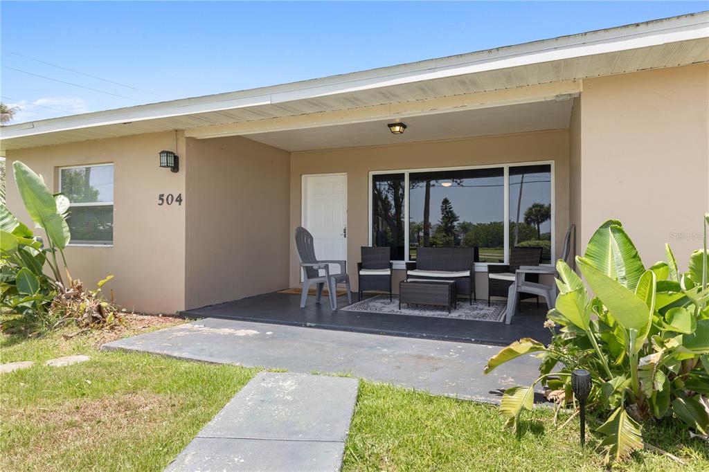 A beige house exterior features a covered front porch with patio furniture and a walkway — 504 RIVERSIDE DRIVE, HOLLY HILL, FL