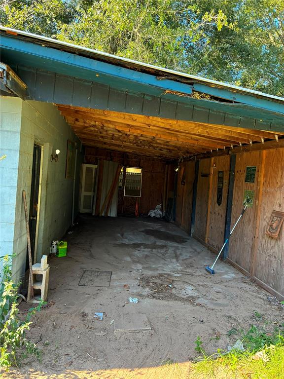 An open-air carport with a concrete floor, wooden ceiling beams, and plywood wall panels — 17990 SE 51ST STREET, OCKLAWAHA, FL