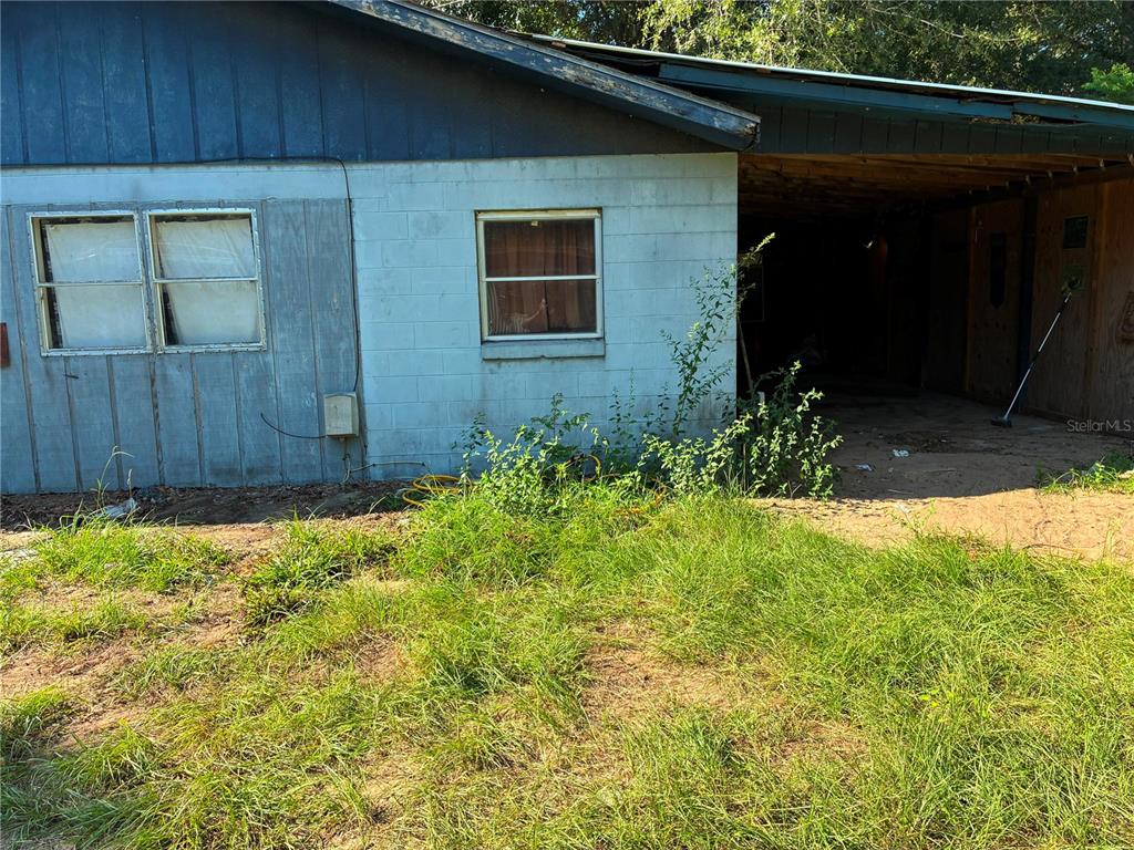 The exterior of a house features a concrete block wall, a carport, and overgrown grass — 17990 SE 51ST STREET, OCKLAWAHA, FL