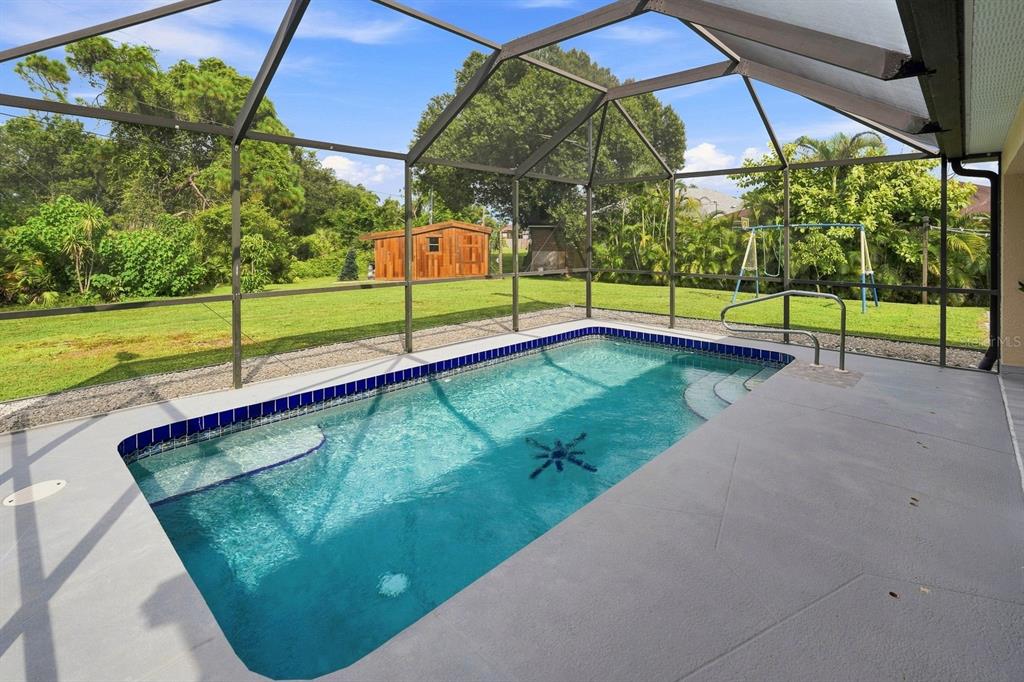 A screened-in swimming pool with a blue tile border sits on a concrete patio — 7570 CROCK AVENUE, NORTH PORT, FL