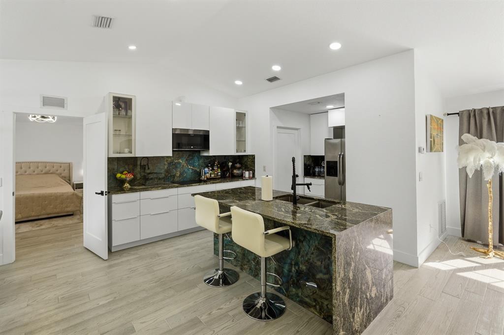 A modern kitchen features a dark stone island, white cabinetry, and light wood-look flooring — 7570 CROCK AVENUE, NORTH PORT, FL