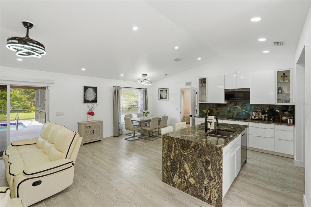 An open-concept kitchen and living area features white cabinetry, a granite island, and wood-look flooring — 7570 CROCK AVENUE, NORTH PORT, FL