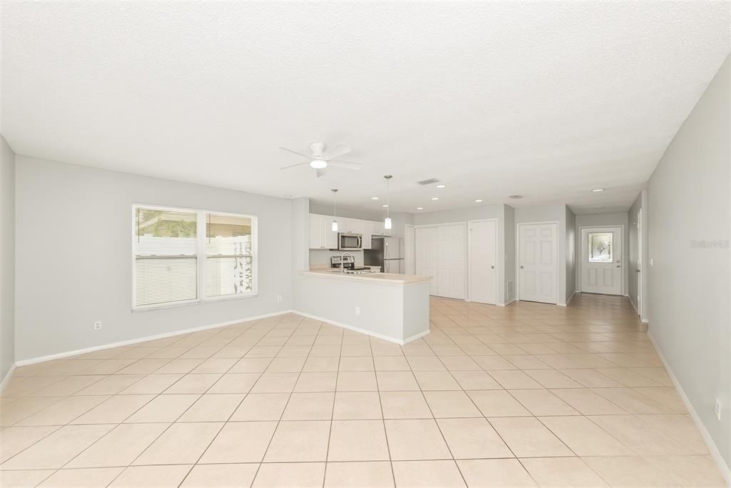 An open-concept living and kitchen area with light-colored tile flooring and white cabinetry — 1215 39TH STREET W, BRADENTON, FL