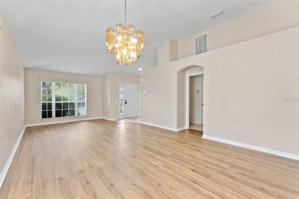 An empty living room features light wood-look flooring, a vaulted ceiling, and a modern chandelier — 30407 STAPLETON STREET, WESLEY CHAPEL, FL
