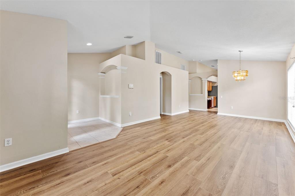 An open-concept living and dining area features light-colored walls, wood-look flooring, and arched architectural details — 30407 STAPLETON STREET, WESLEY CHAPEL, FL
