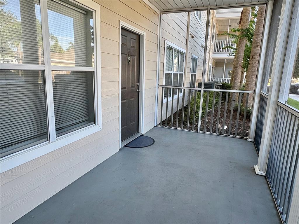 A screened-in porch features a dark brown entry door, gray flooring, and beige siding — 4802 51ST STREET W UNIT 102, BRADENTON, FL