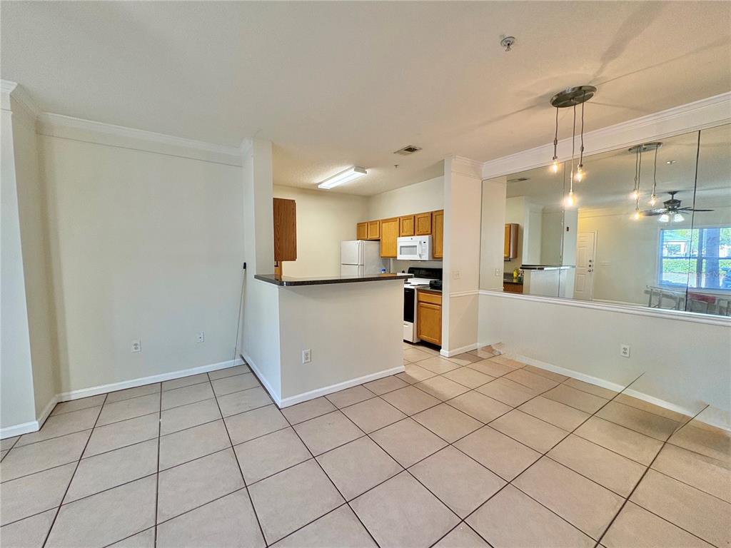 A kitchen with wood cabinets and a breakfast bar opens to a tiled dining area — 4802 51ST STREET W UNIT 102, BRADENTON, FL